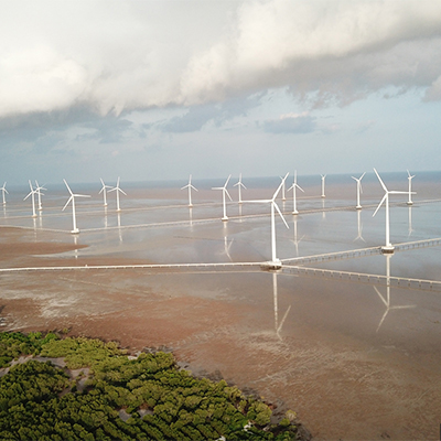 Aerial view of offshore wind turbines and coastal greenery.