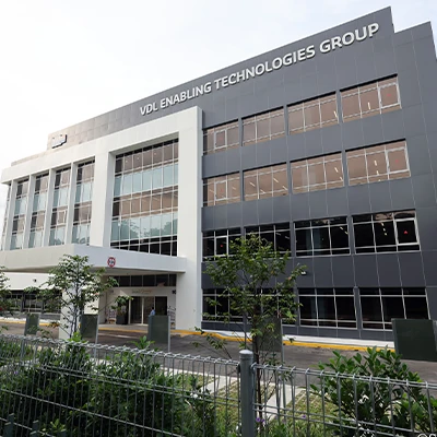 Exterior view of the VDL Enabling Technologies Group building, a modern multi-story facility with large glass windows and sleek gray paneling.