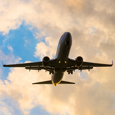 Airplane in flight captured from below against a cloudy sky during sunset.