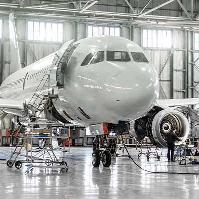 Aircraft undergoing maintenance in a hangar, with engineers working on its engines and systems.