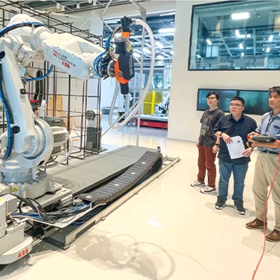 Three engineers observe and operate a large industrial robotic arm inside a high-tech lab environment, with advanced machinery and equipment in the background.